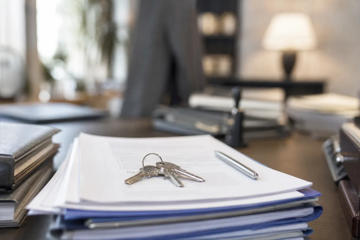 Documents de vente immobilière et clés de maison posés sur le bureau d&rsquo;une étude notariale